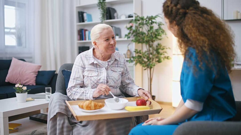 Older adults and family members share a holiday meal beside simple decorations in a bright common room.