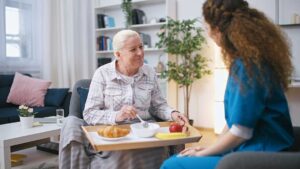 Older adults and family members share a holiday meal beside simple decorations in a bright common room.