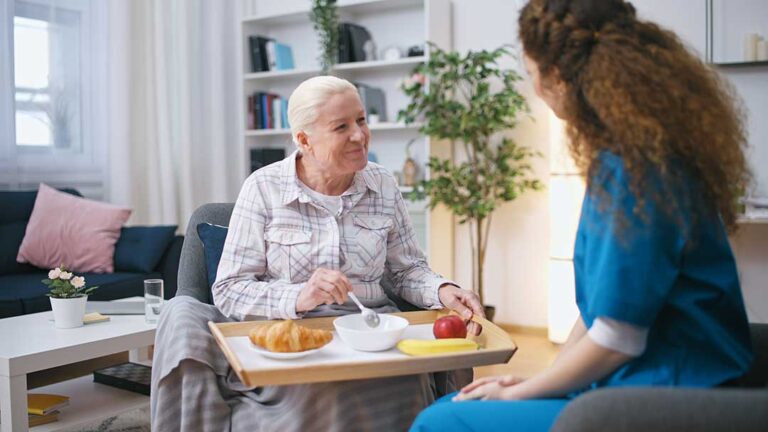 Older adults and family members share a holiday meal beside simple decorations in a bright common room.