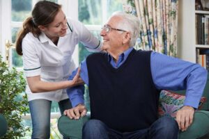 A caregiver assists an older adult with taking daily prescription pills at a well-lit table.