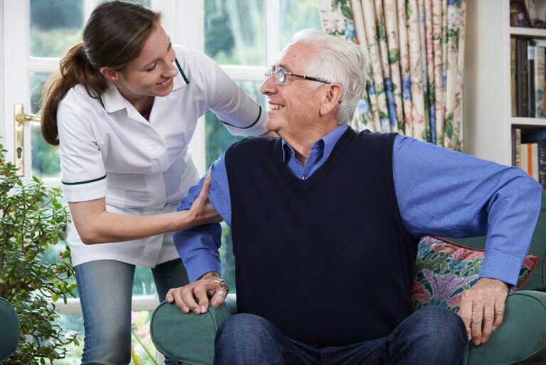 A caregiver assists an older adult with taking daily prescription pills at a well-lit table.